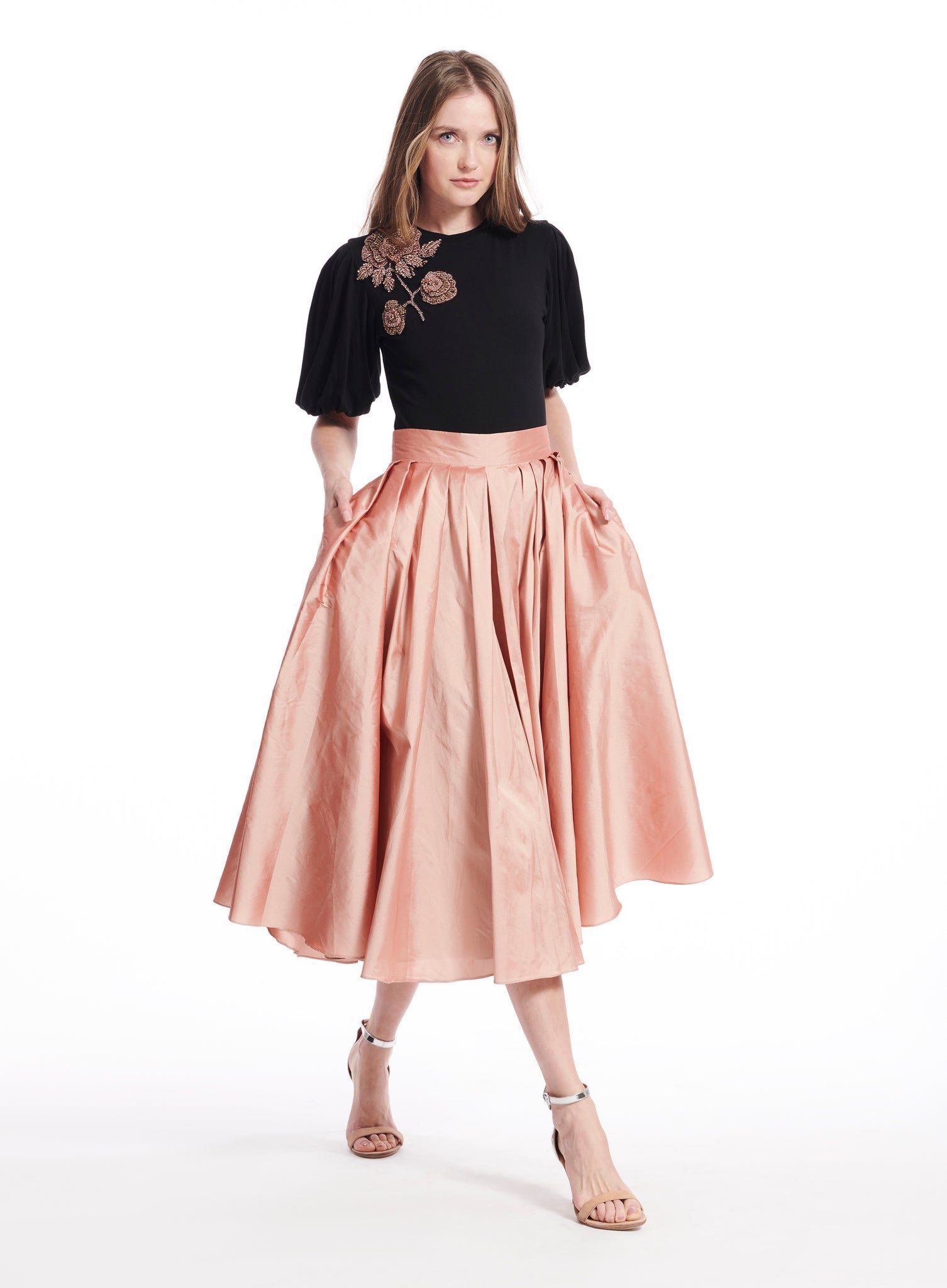 A woman is wearing a black top and a pink skirt.