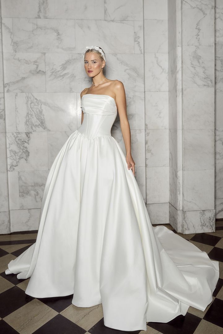 A woman in a white wedding dress is standing in front of a checkered floor.
