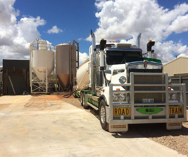 A Yellow And Black Construction Vehicle Is Driving Through A Dirt Field — Frontier Cement Supplies In Broome, NT