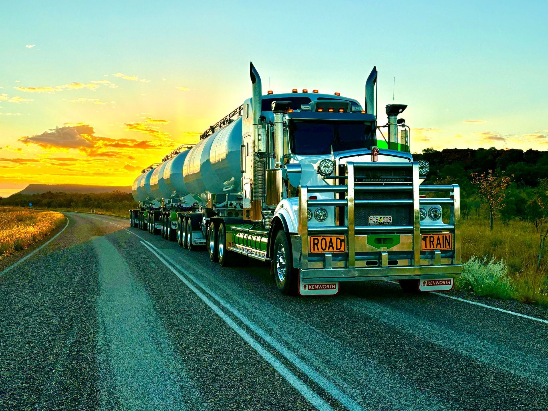 Semi-truck with tanker trailers driving on a road at sunset, with orange and blue sky — Frontier Cement Supplies In East Arm, NT