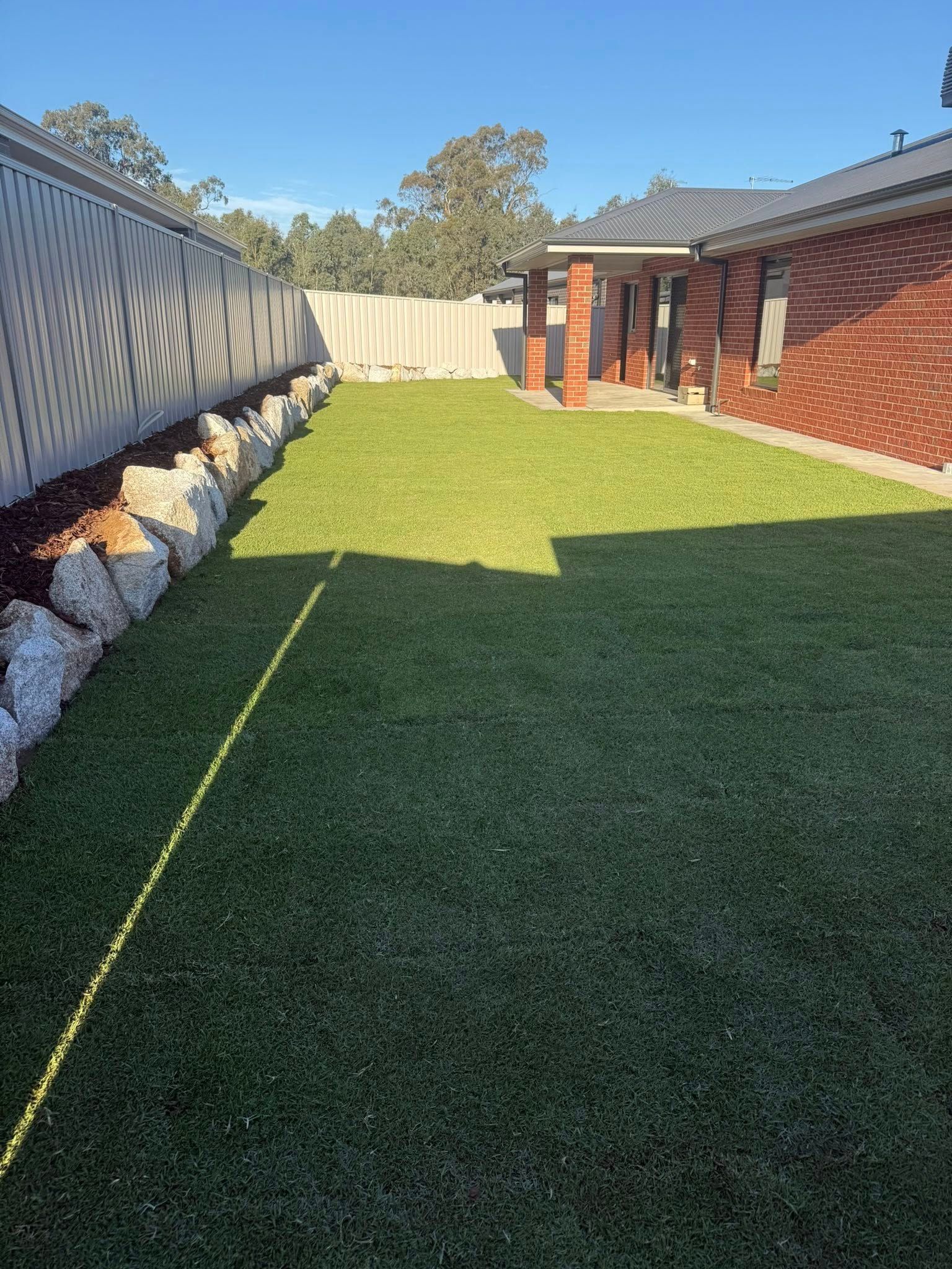 Retaining Walls With Green Lawn, and Brick House — Robbo's Hire In Thurgoona, NSW