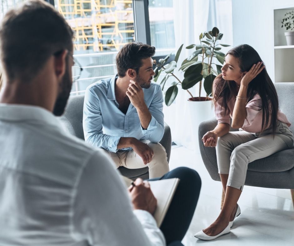 A young seated couple resolving their differences with the help of a mediator who is sitting opposite