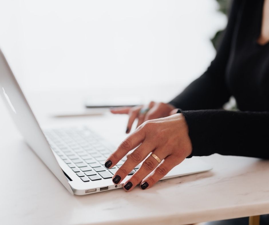 close up of womans's hands poised over laptop keys