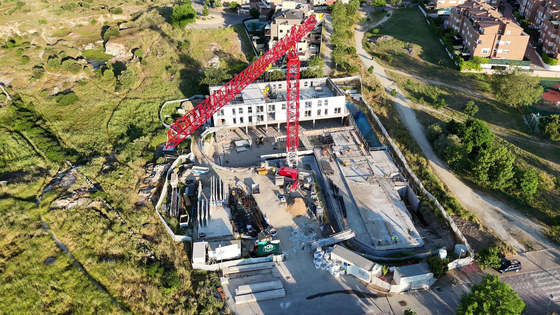Sitio de construcción con una grúa roja levantando materiales hacia un edificio.