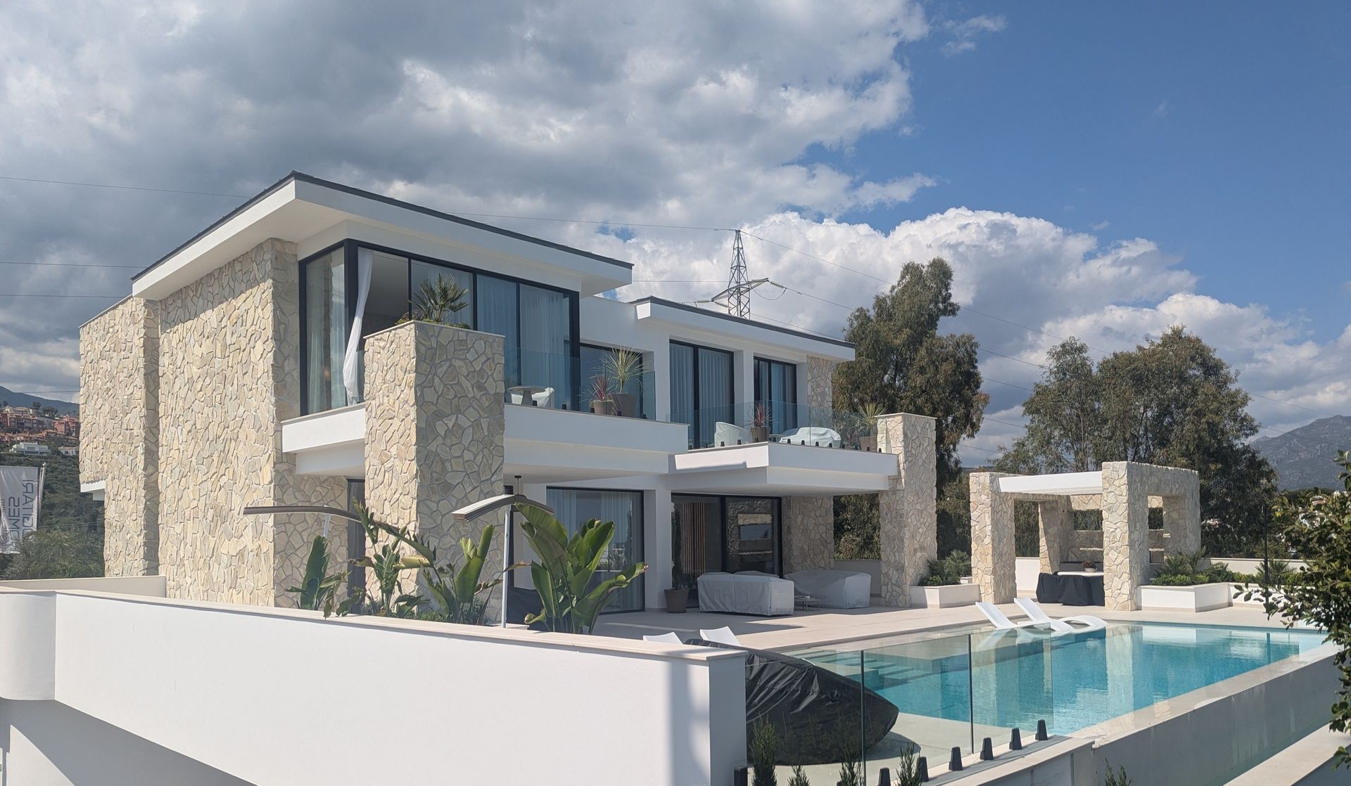 Moderna casa de lujo con piscina, paredes blancas, detalles de piedra y cielo azul.