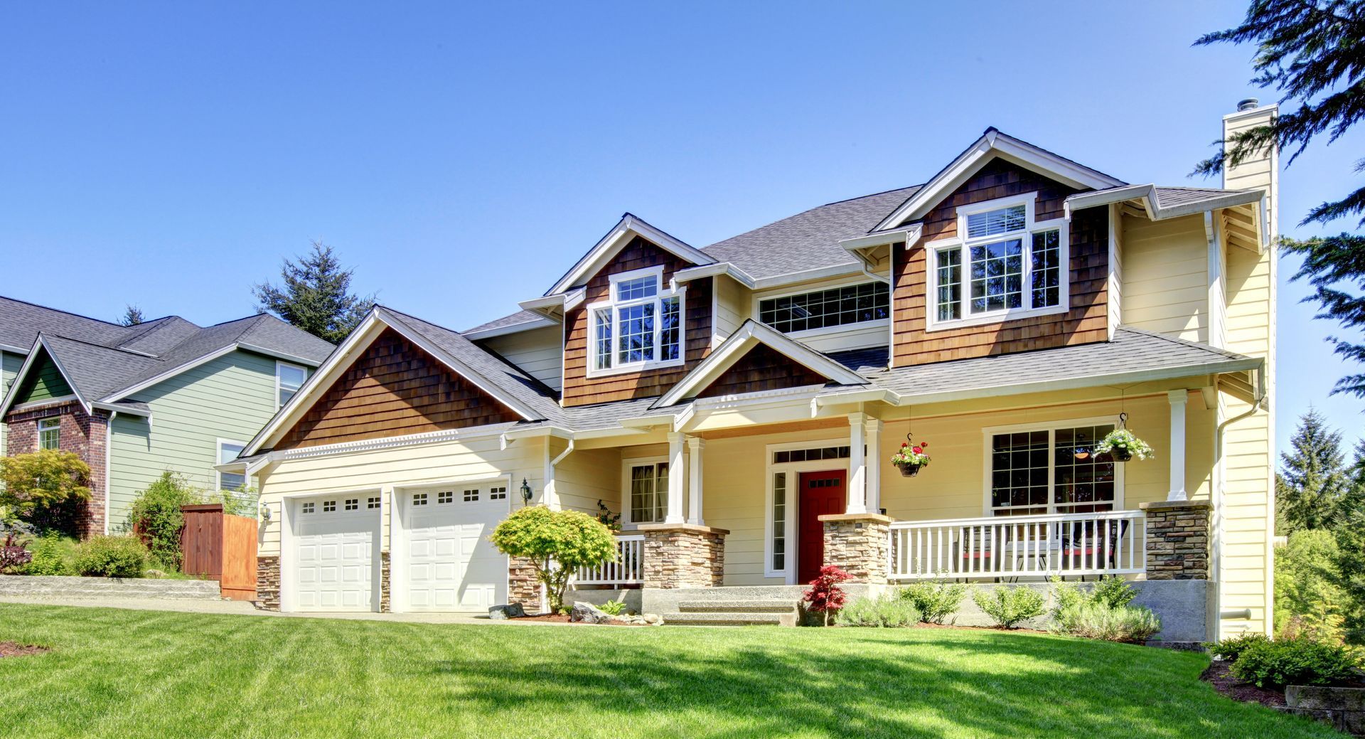 Suburban house with two garage doors, beige siding, dormer windows, and a green lawn in front.