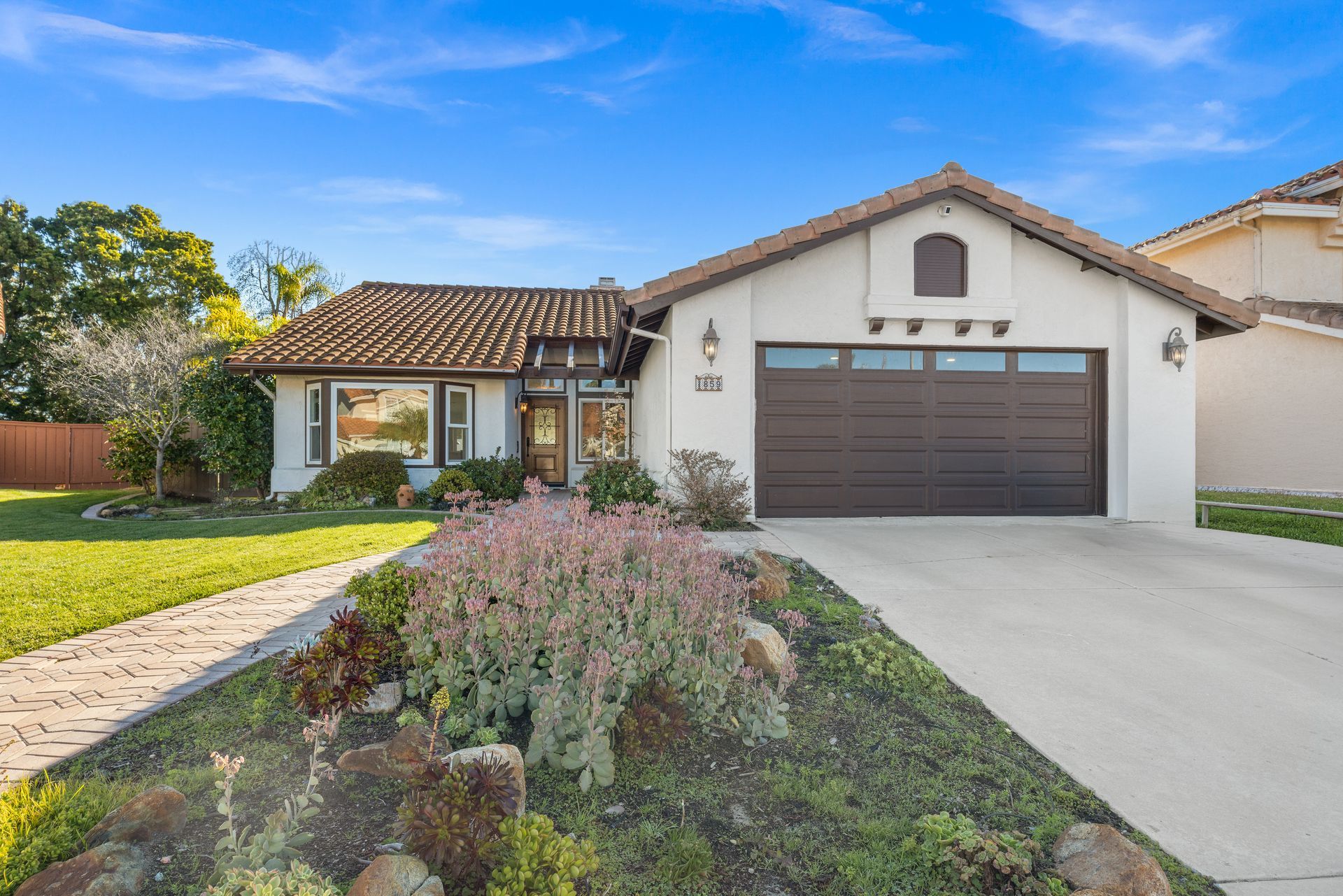 Suburban house with a brown garage door, white stucco exterior, driveway, and landscaped front yard