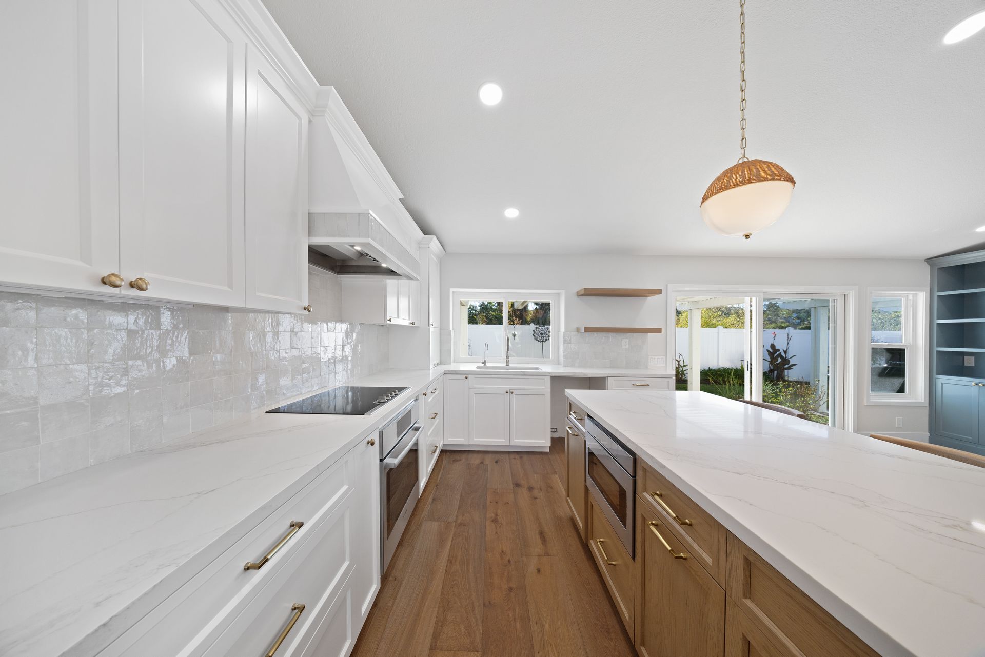 Bright modern white kitchen with wood island, stainless stove, and sliding glass doors to patio