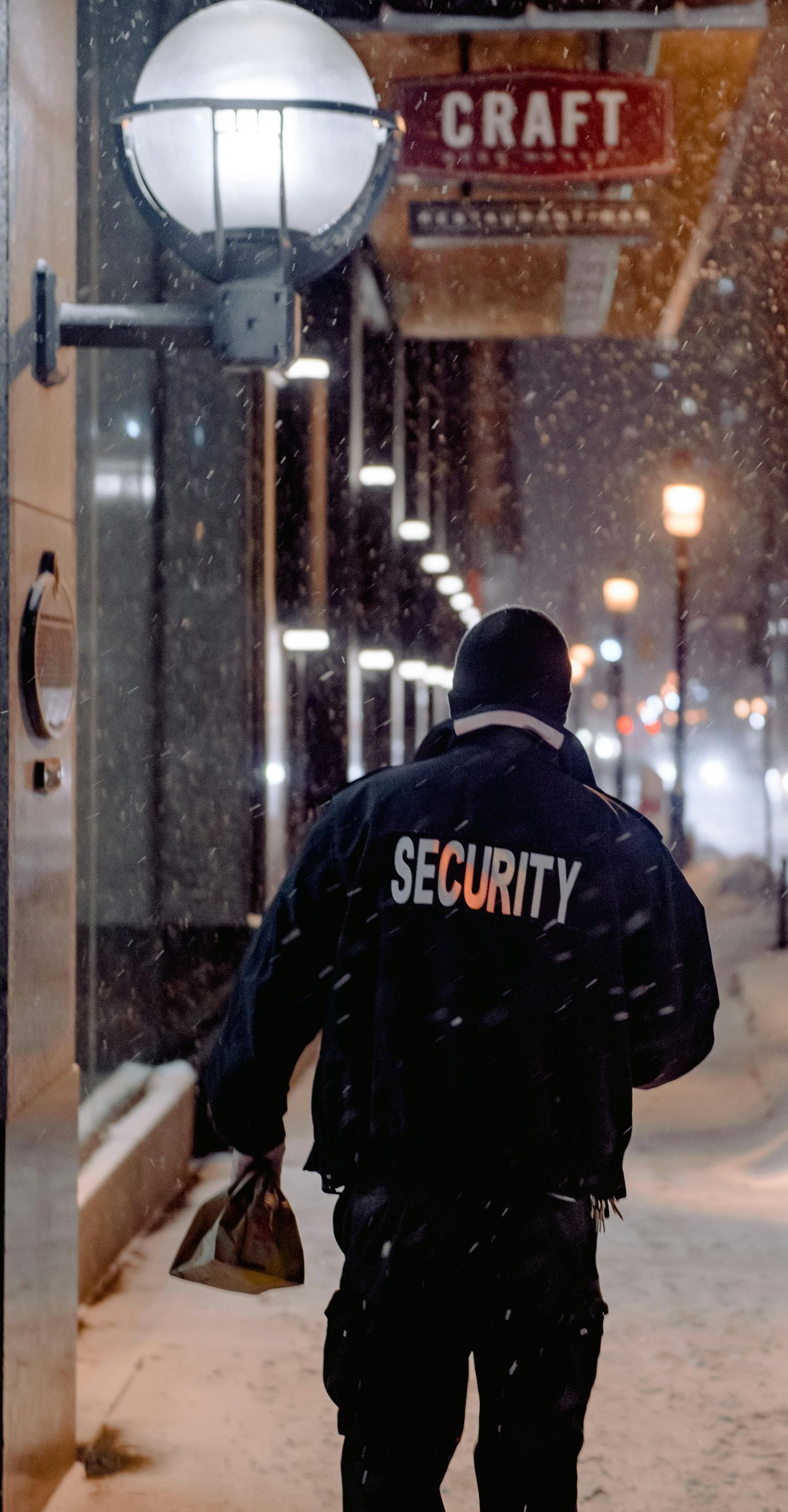 A security guard is walking down a snowy sidewalk.