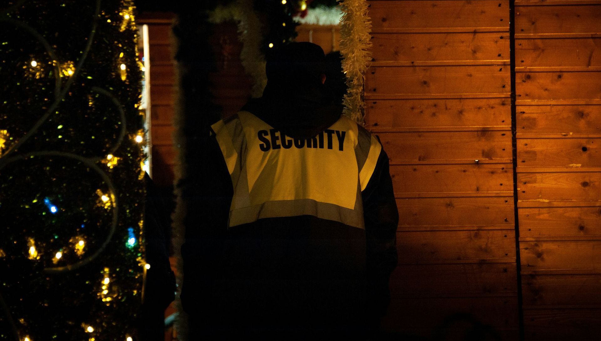 A security guard is standing in front of a christmas tree.