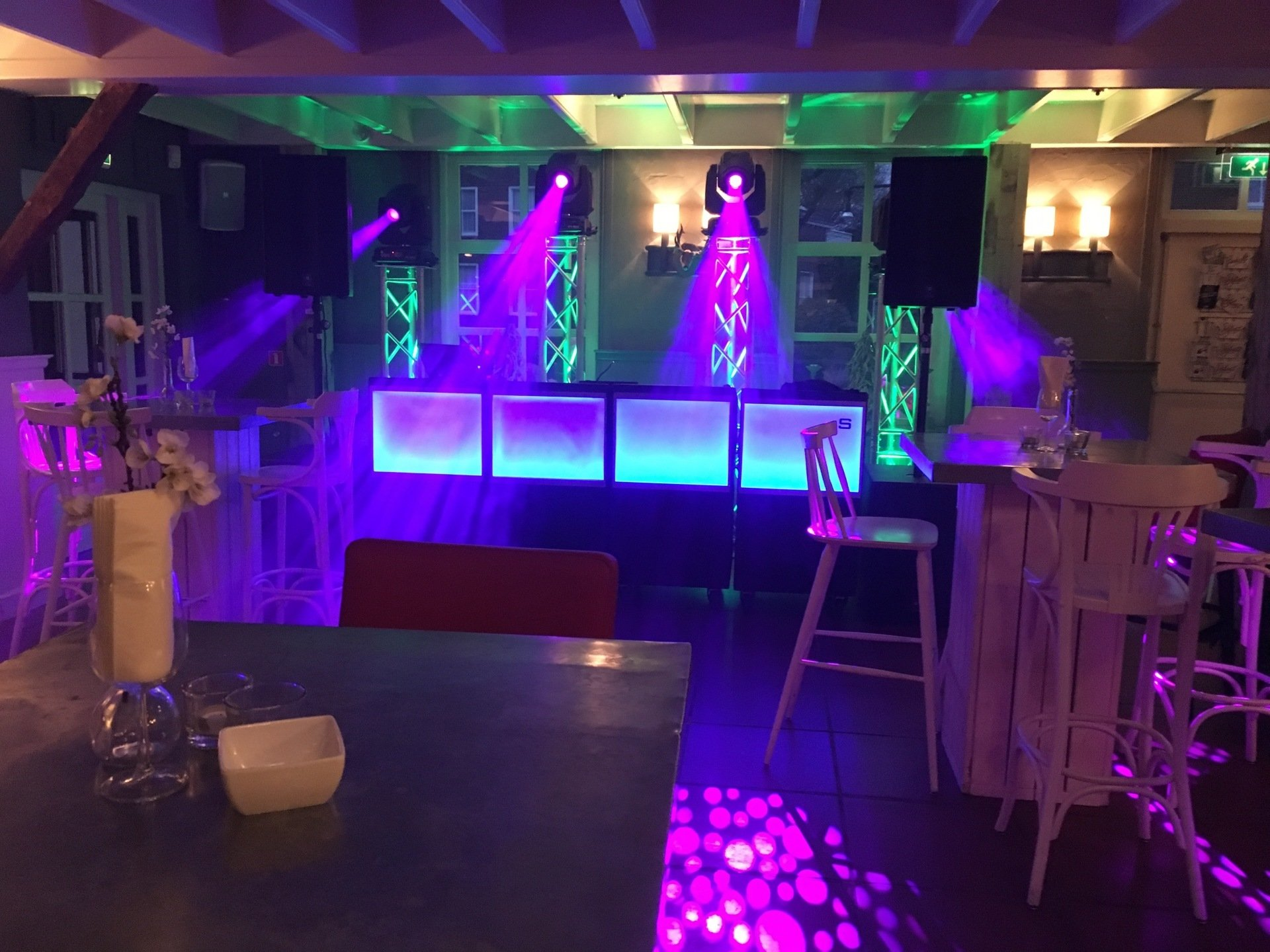 Paars verlicht nachtclubpodium met lege tafels en stoelen op de voorgrond.