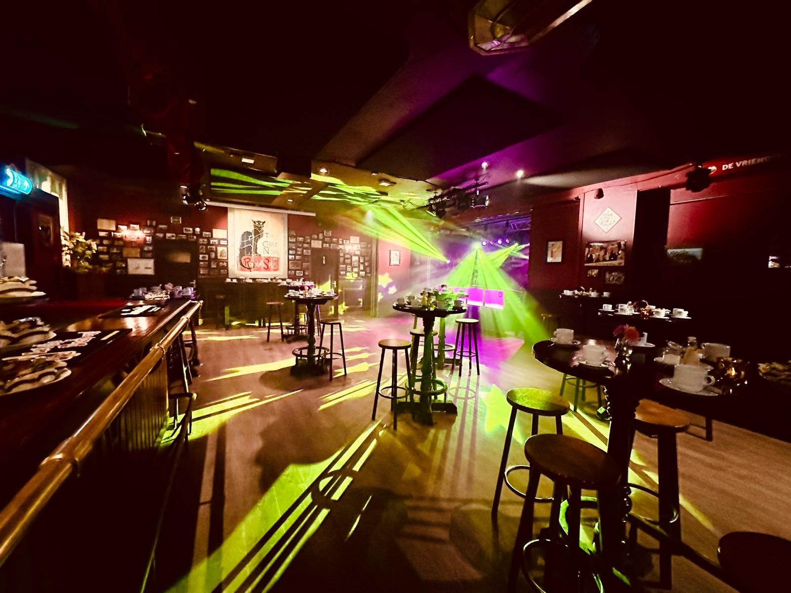Een lege nachtclub met groene en paarse laserlichten boven de tafels en krukken.