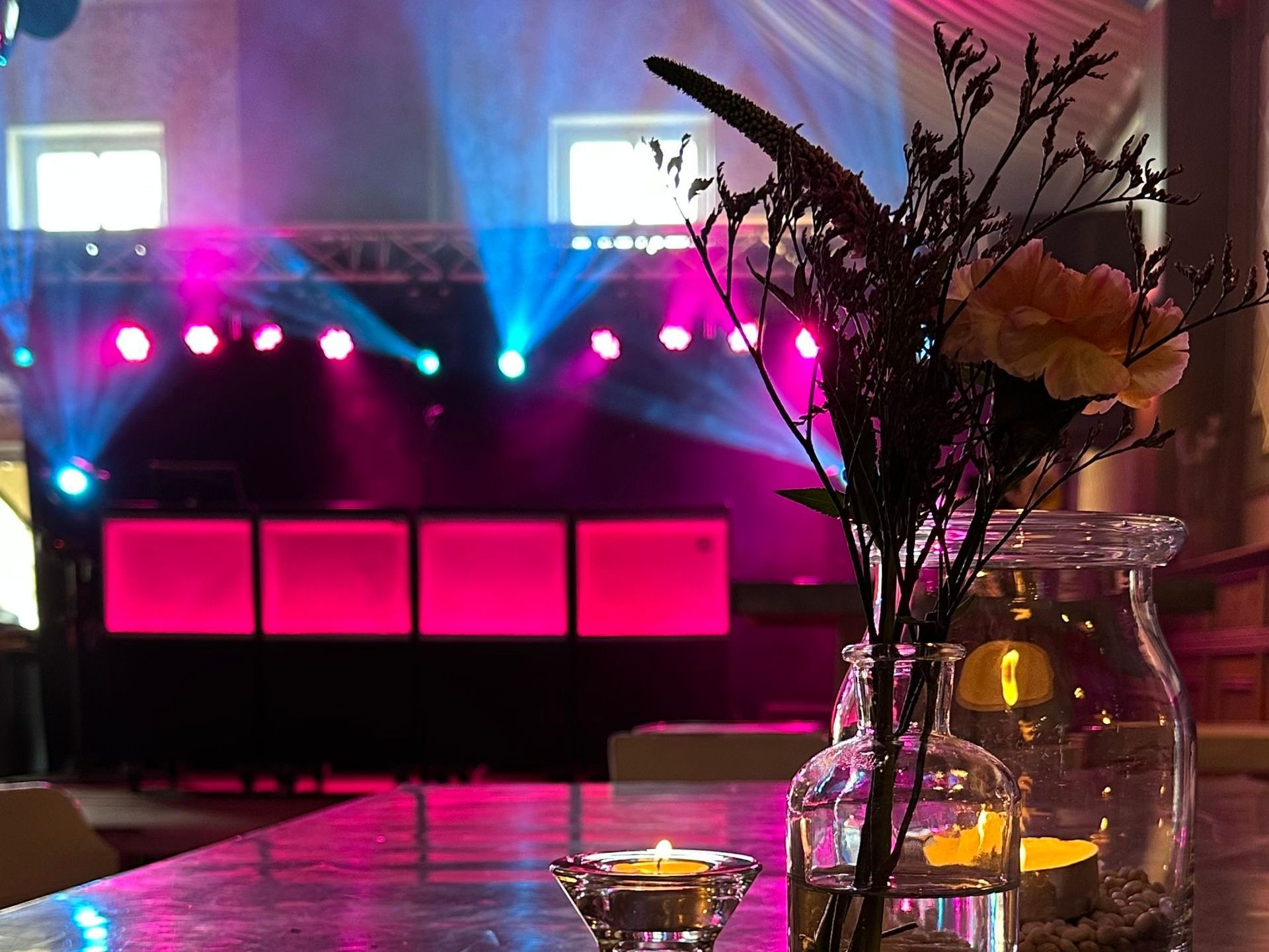 Een schemerig verlicht podium met roze en blauwe lampen, een tafel en een bloemstuk op de voorgrond.