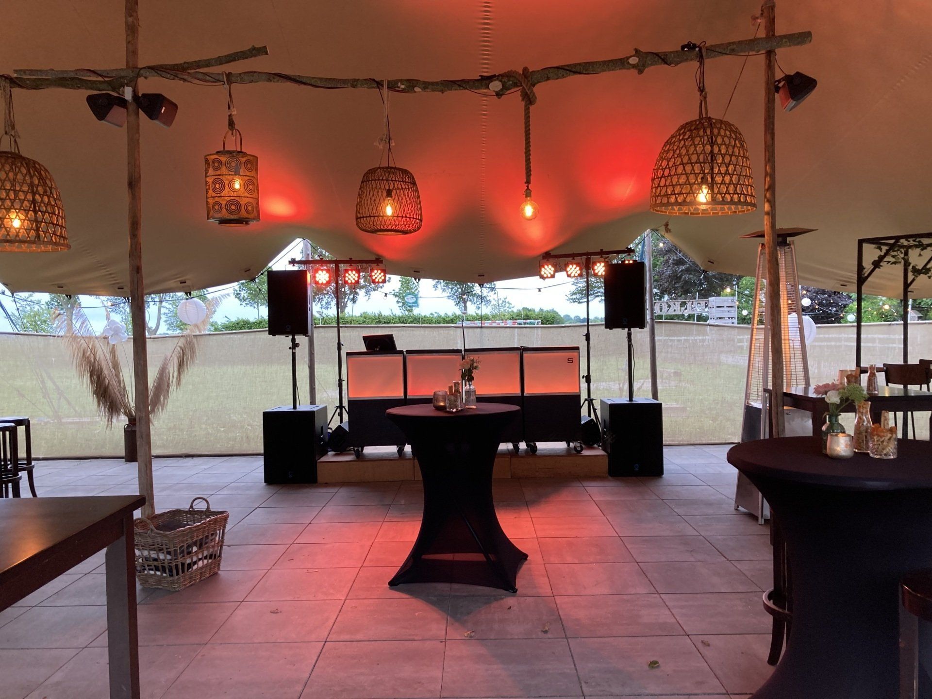 Openluchtterras met hangende lantaarns, warme oranje verlichting en cocktailtafels bij schemering