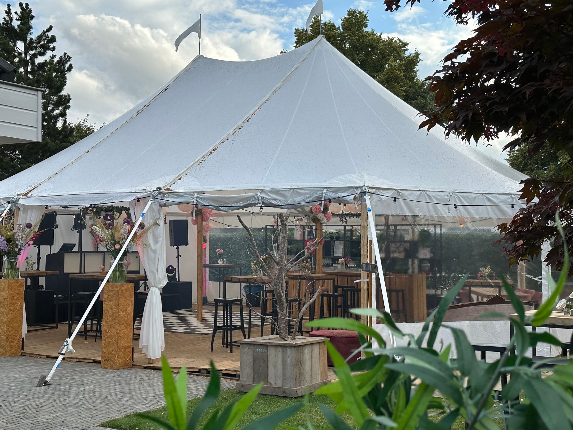 Witte evenemententent voor buiten met open zijkanten, tafels en stoelen in een tuinachtige omgeving.