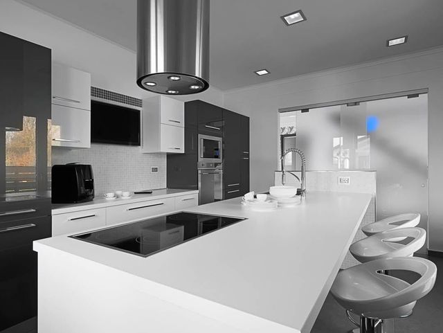 Modern white kitchen with island, bar stools, stainless appliances, and pendant lights