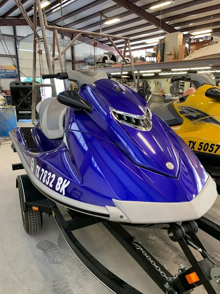 Blue and white jet ski on a trailer inside a warehouse, with a yellow jet ski behind it
