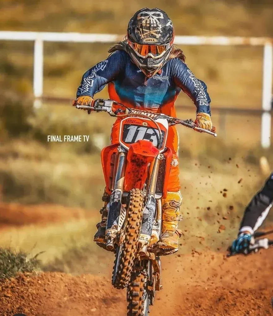 Motocross rider on an orange dirt bike jumping through a dirt track