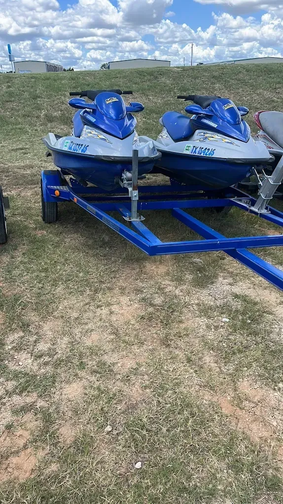 Blue jet skis on a trailer parked on grass under a cloudy sky