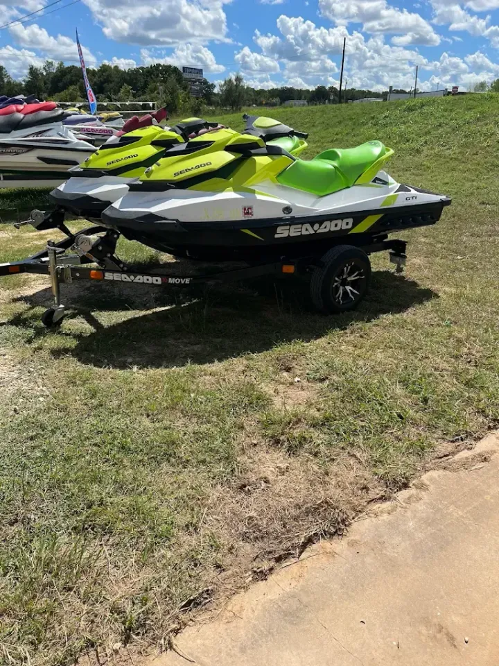 Three Sea-Doo jet skis on a trailer in a grassy lot under a partly cloudy sky