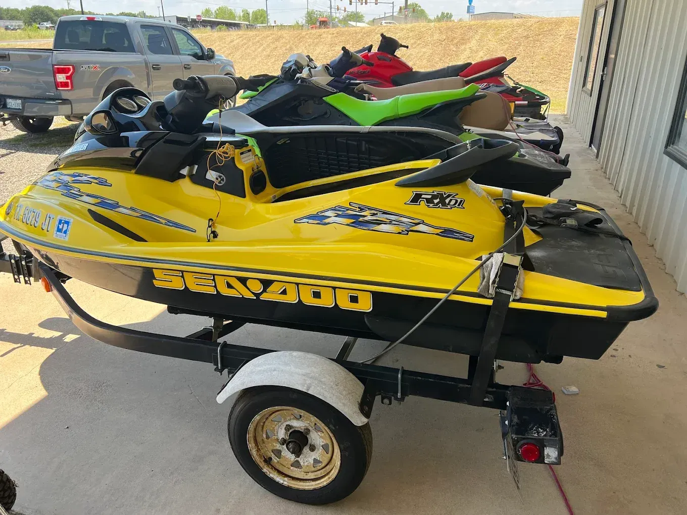 Yellow jet ski on a trailer beside a building, with two other jet skis stacked on top.