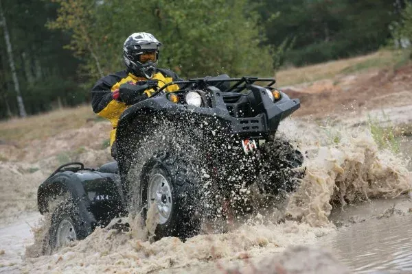 ATV rider splashes through muddy water on a dirt trail in the woods