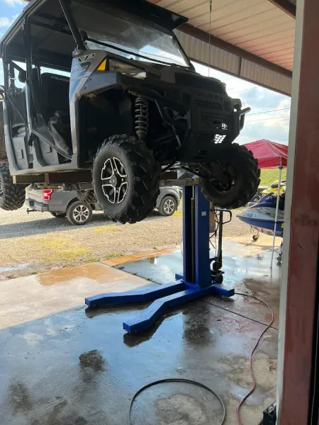 Black off-road vehicle lifted on a blue hydraulic hoist in a garage.
