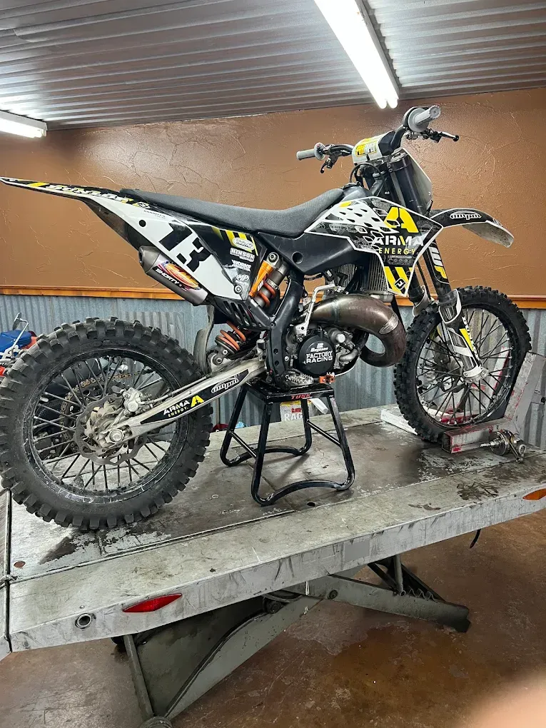 Yellow and black dirt bike on a stand in a garage or workshop, with mud-covered tires and frame