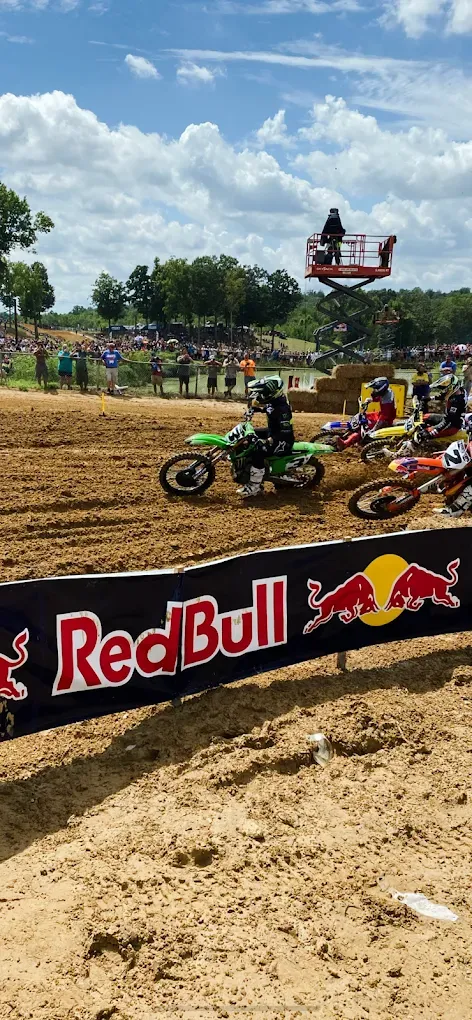Motocross rider airborne over dirt track with Red Bull banner and spectators in the background
