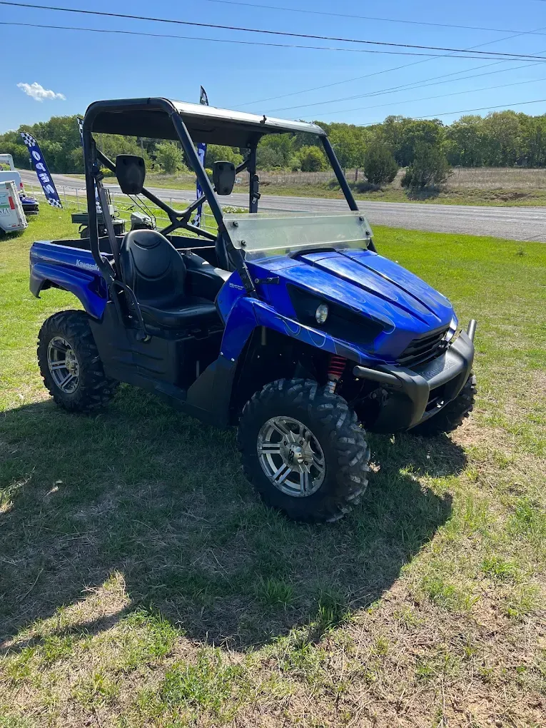 Blue off-road utility vehicle parked on grass under a sunny sky