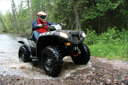 Person riding a black ATV through a muddy forest trail