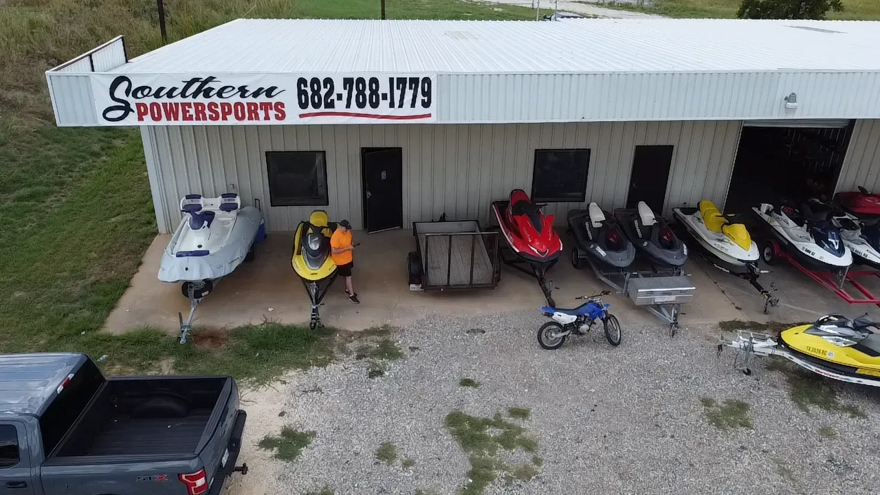 Aerial view of a waterfront powersports shop with jet skis, boats, and a person standing outside.