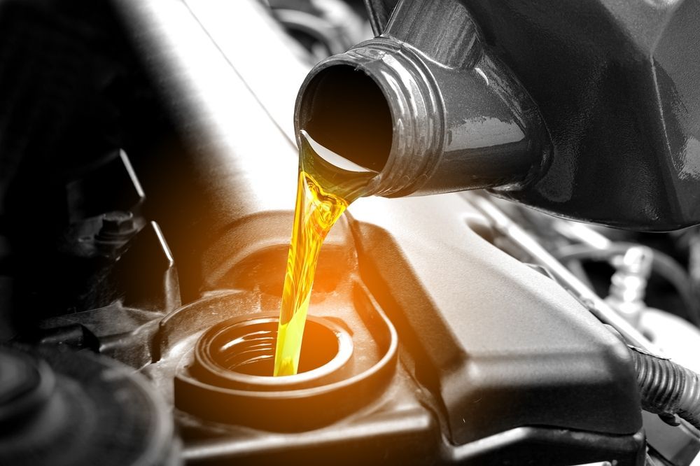 Motorcycle engine oil being poured into a filler opening, with warm orange liquid and black metal parts.
