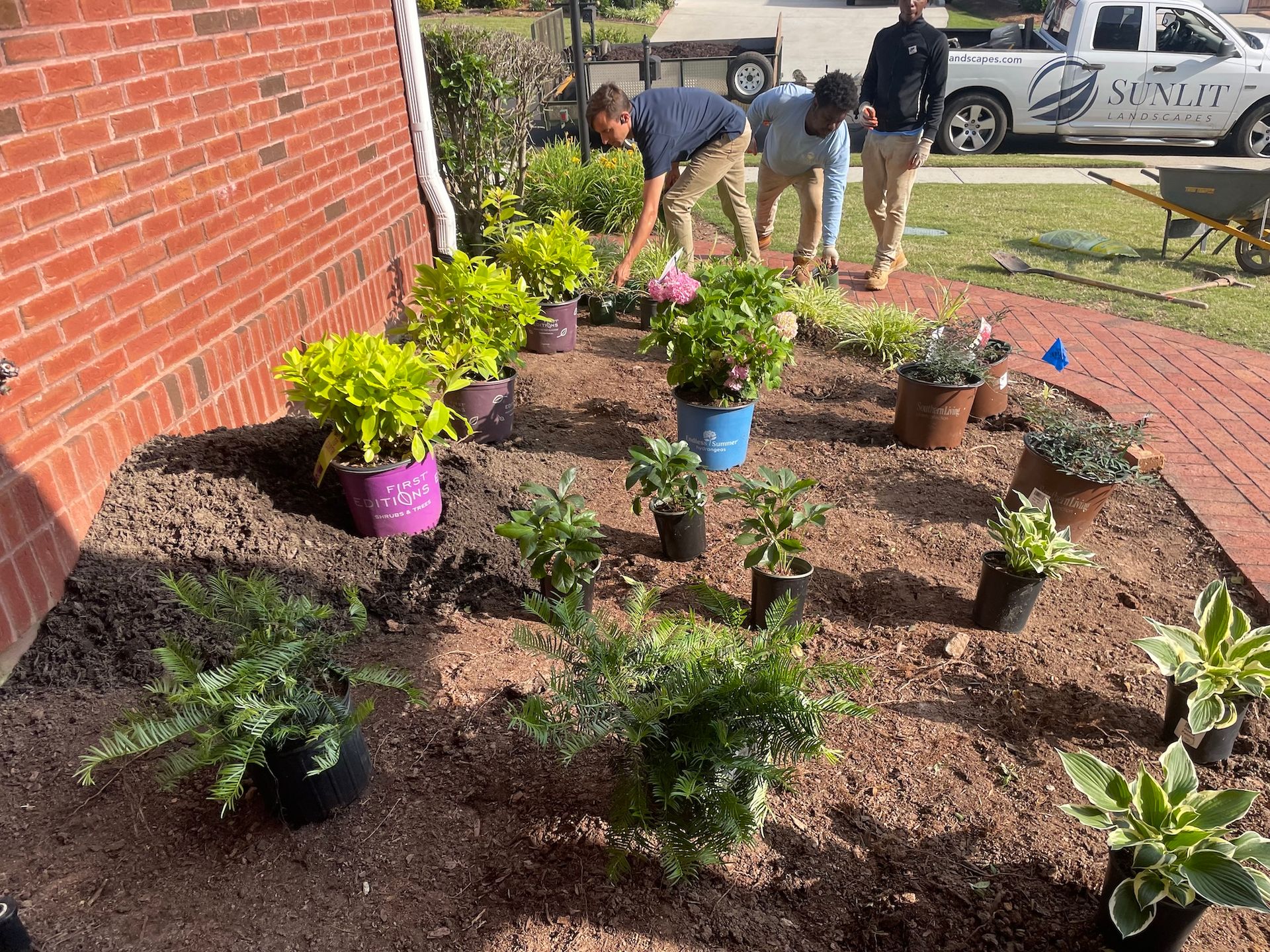Landscapers planting flowers in a garden bed next to a brick building.