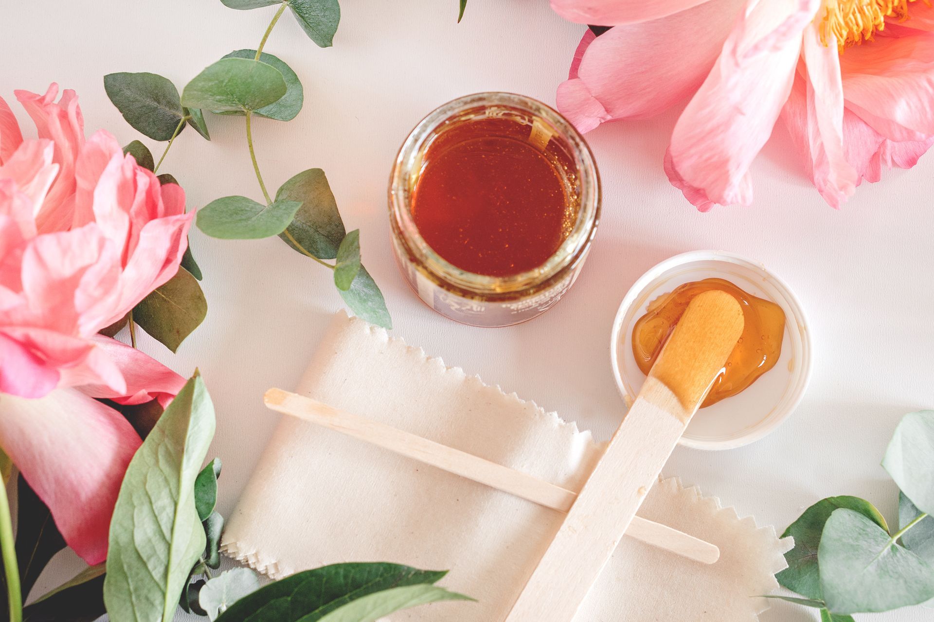 Pink flowers, leaves, and jars of honey and honey dipper on a soft pastel background