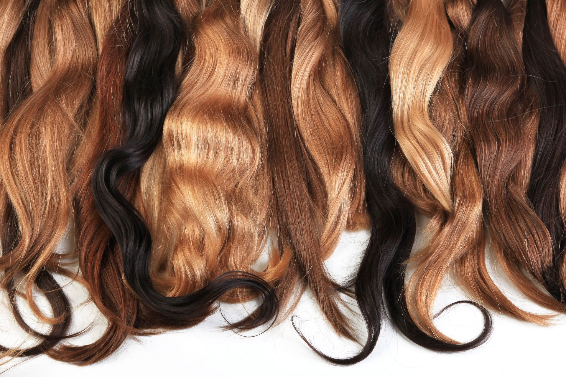 Long wavy hair extensions in brown and blonde shades arranged on a white background