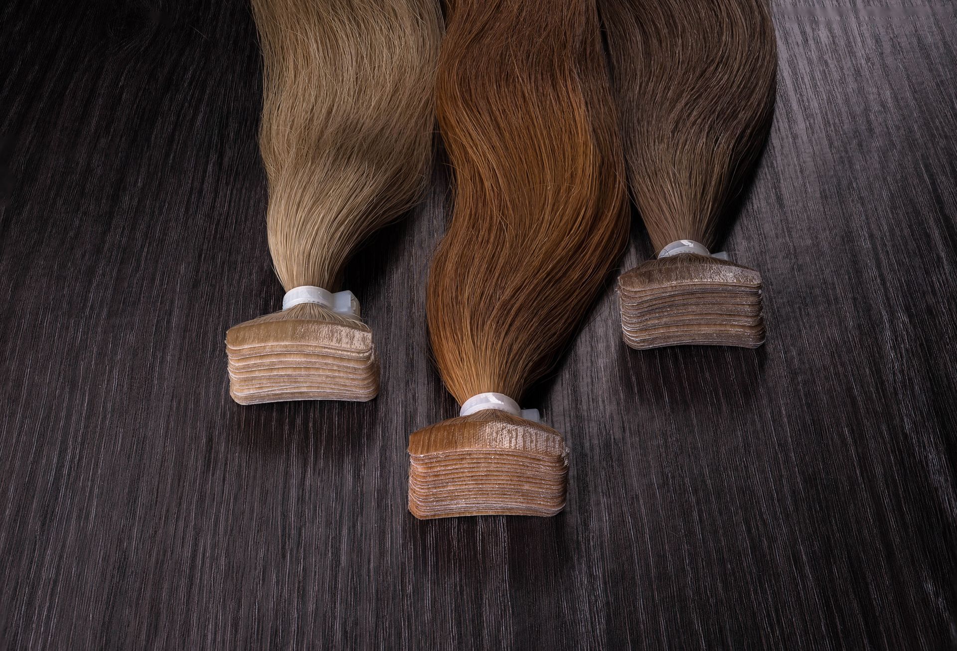 Three horse tails with braided ends resting on a dark textured surface