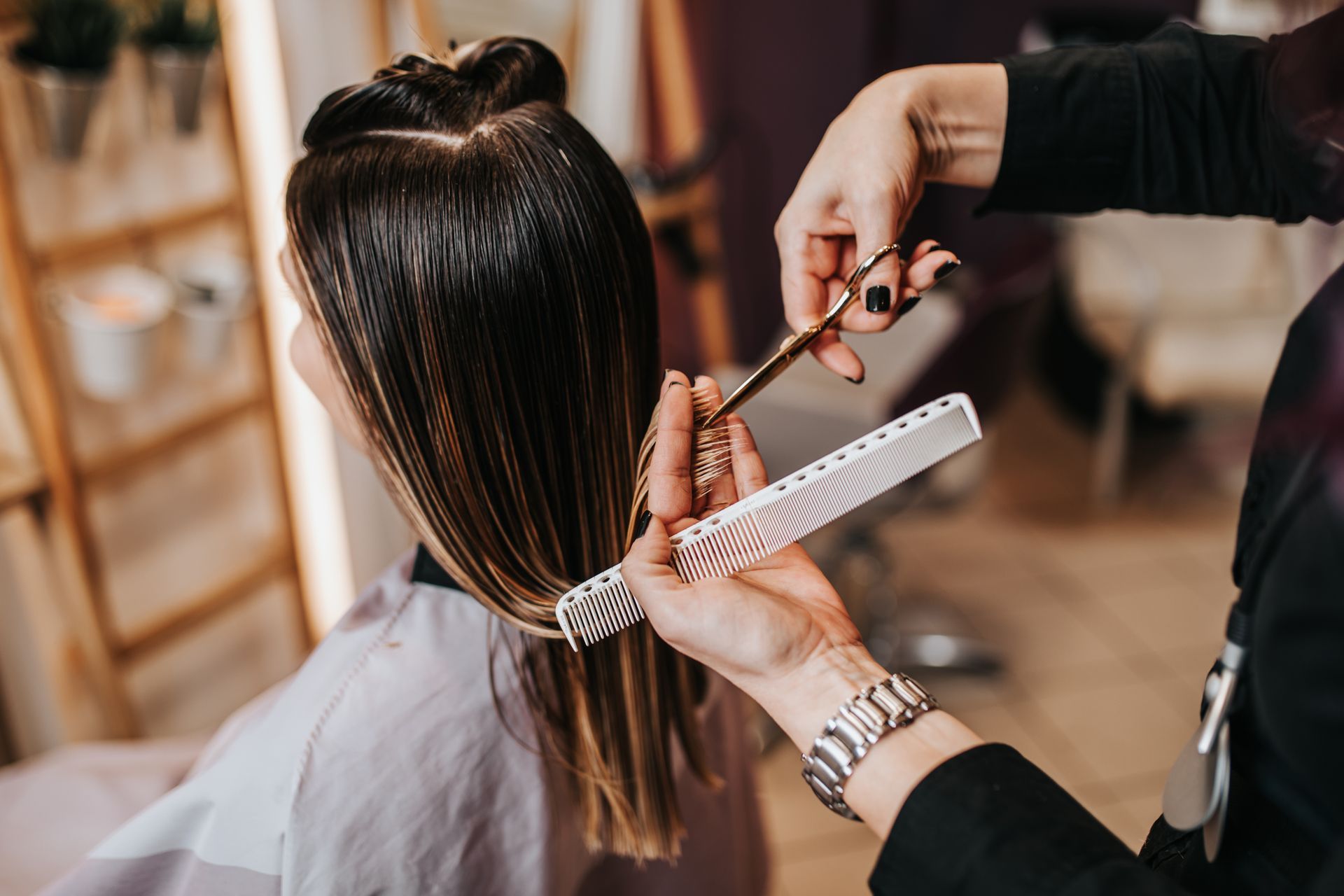 Hairdresser cutting a client’s long dark hair with scissors and comb in a salon Hairdresser cutting a client’s long dark hair with scissors and comb in a salon