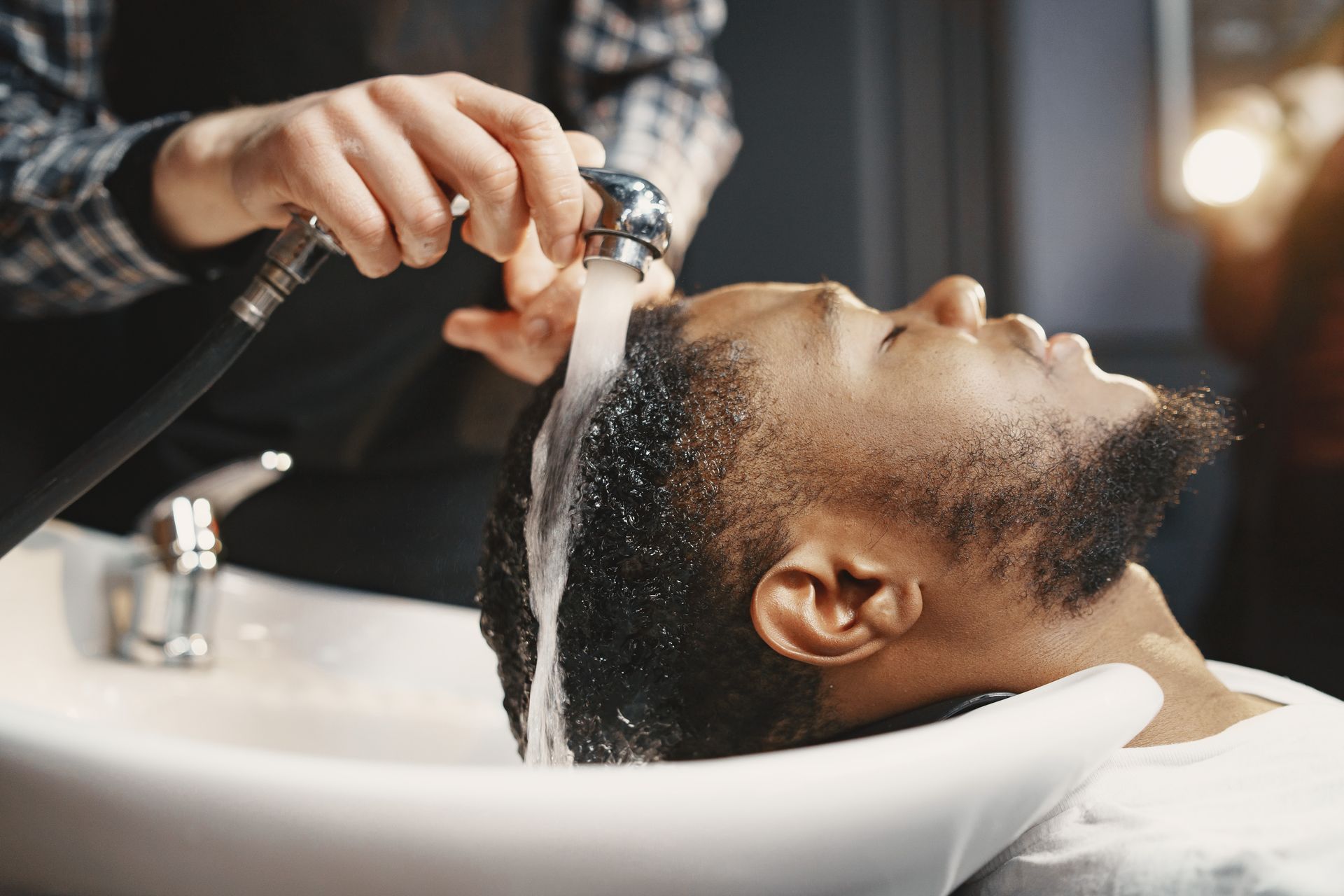 Hair washing at a salon sink, with water rinsing over a client’s head Hair washing at a salon sink, with water rinsing over a client’s head