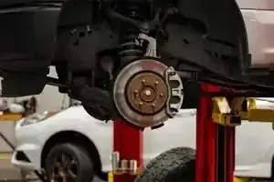 Car wheel removed on lift, exposing brake rotor and suspension in a garage.