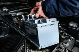 Hand placing a battery into a car engine bay