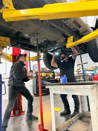 Hands working in a car engine bay, adjusting parts near a red battery terminal.