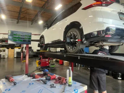 Person adjusting a wheel alignment tool on a car tire at a repair shop