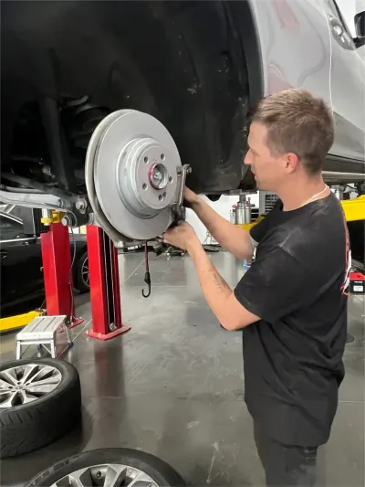 Car wheel hub and brake rotor lifted on a garage hoist, with a white car in the background
