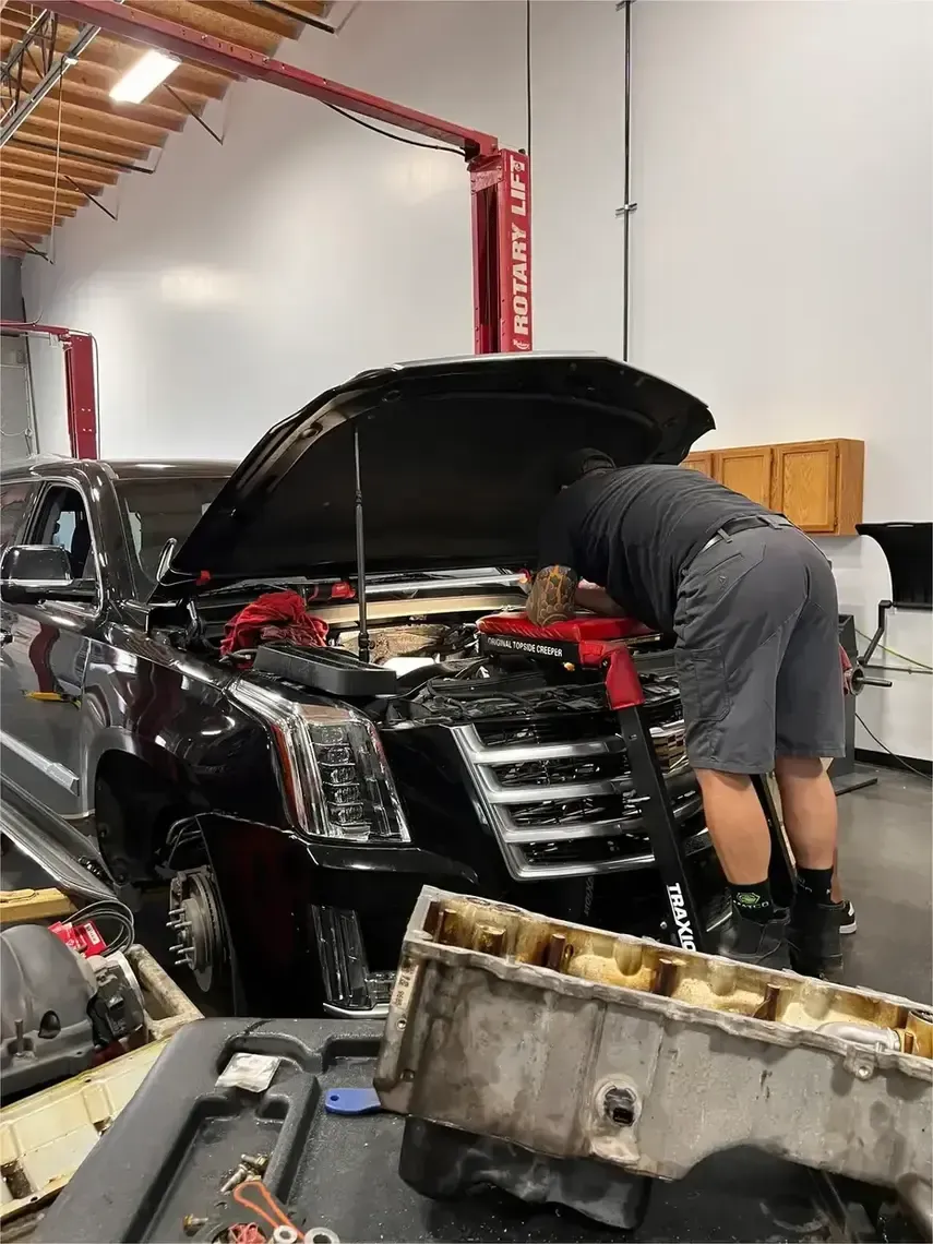 Mechanic leaning into a black SUV’s open hood inside an auto repair shop