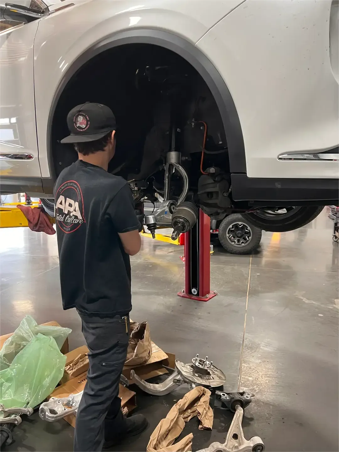Mechanic inspecting the underside of a silver car lifted on a hydraulic jack in an auto shop.