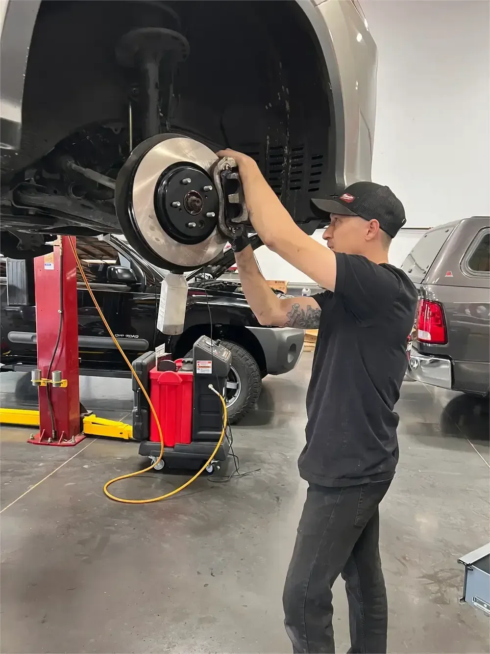 Mechanic working on a raised car brake assembly in an auto shop, using a tool near the wheel hub
