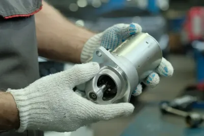 Gloved hands holding a silver metal mechanical part in a workshop