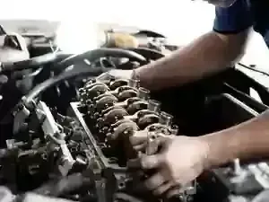 Mechanic working on a car engine, adjusting exposed valve components under the hood