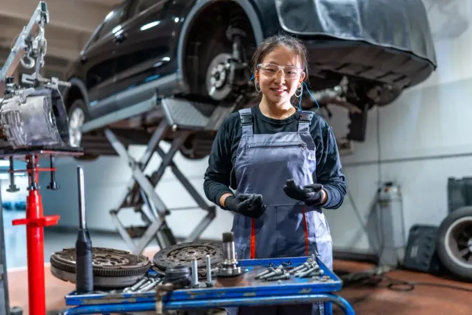 Mechanic in a garage standing by a car on a lift and a workbench with tools